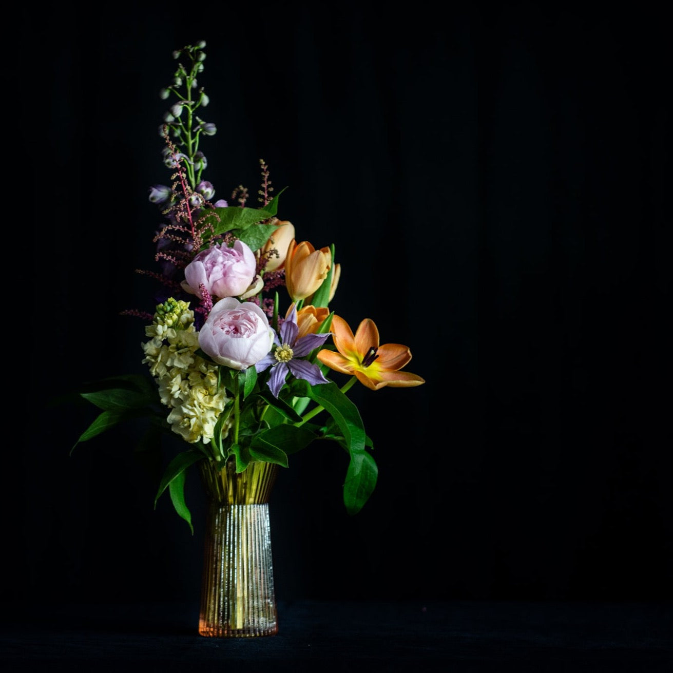 A rose glass bud vase is filled with peonies and spring stems. 