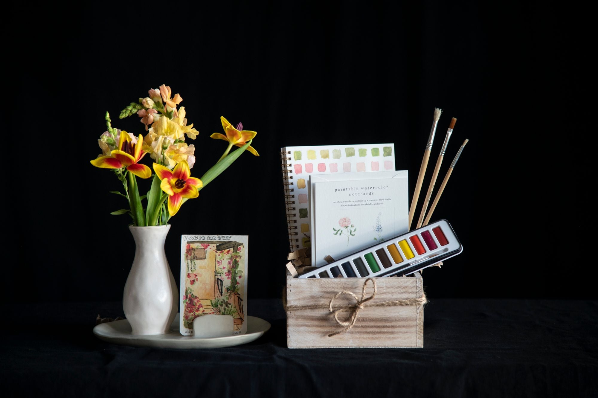 Artistic setup with flowers, paint palette, brushes, and stationery