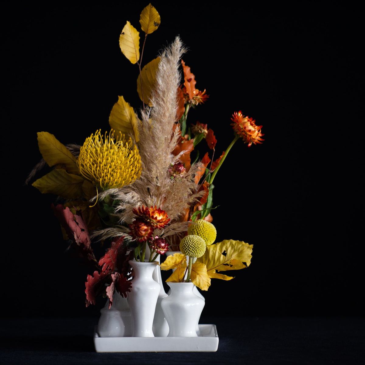 A collection of white ceramic bud vases on a tray filled with seasonal stems.