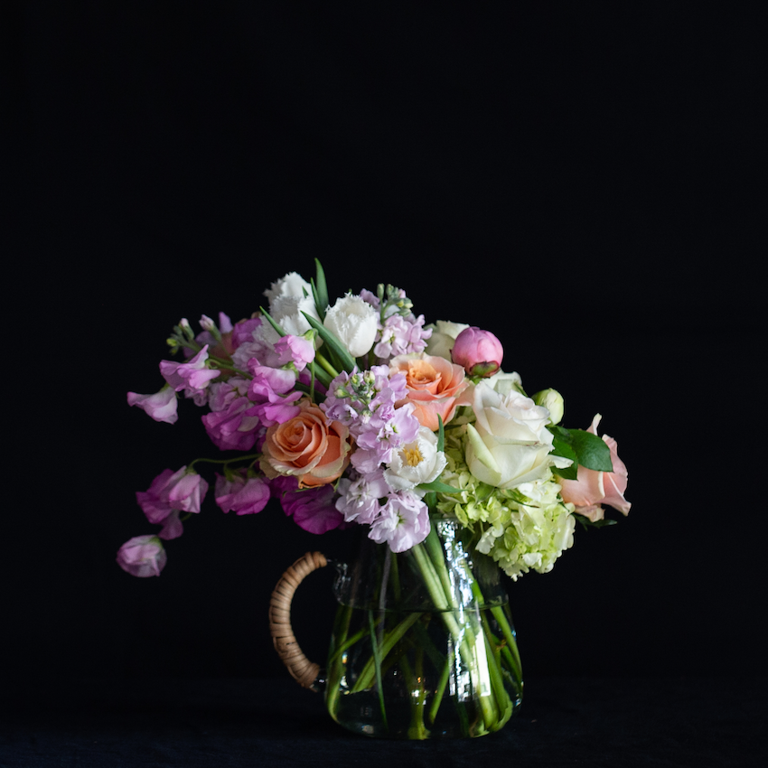 A glass pitcher filled with seasonal stems - hydrangea, roses, tulips, and stock