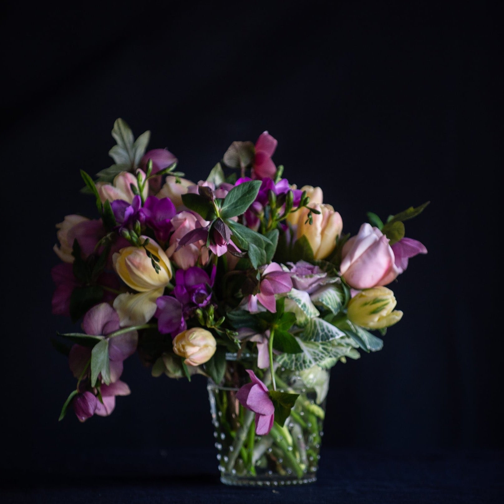 A wild design of tulips, freesia and seasonal stems in a clear vase.