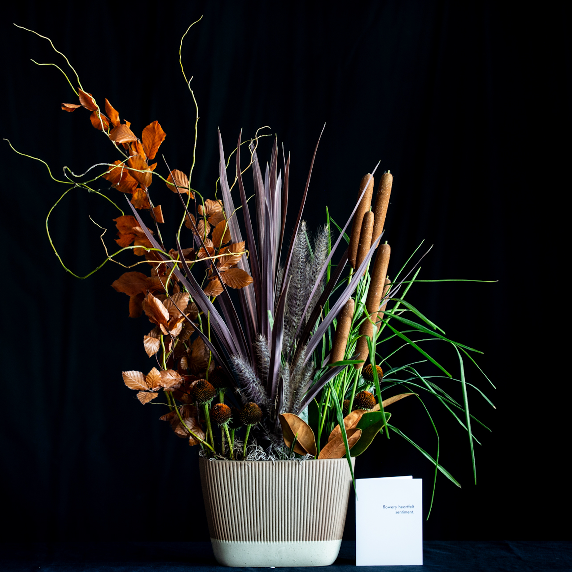 Living plant arrangement with cattails, grasses, rust foliage, and seasonal botanicals in a corrugated ceramic vase