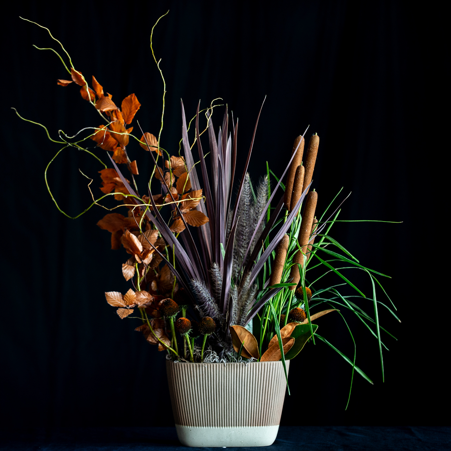 Living plant arrangement with cattails, grasses, rust foliage, and seasonal botanicals in a corrugated ceramic vase