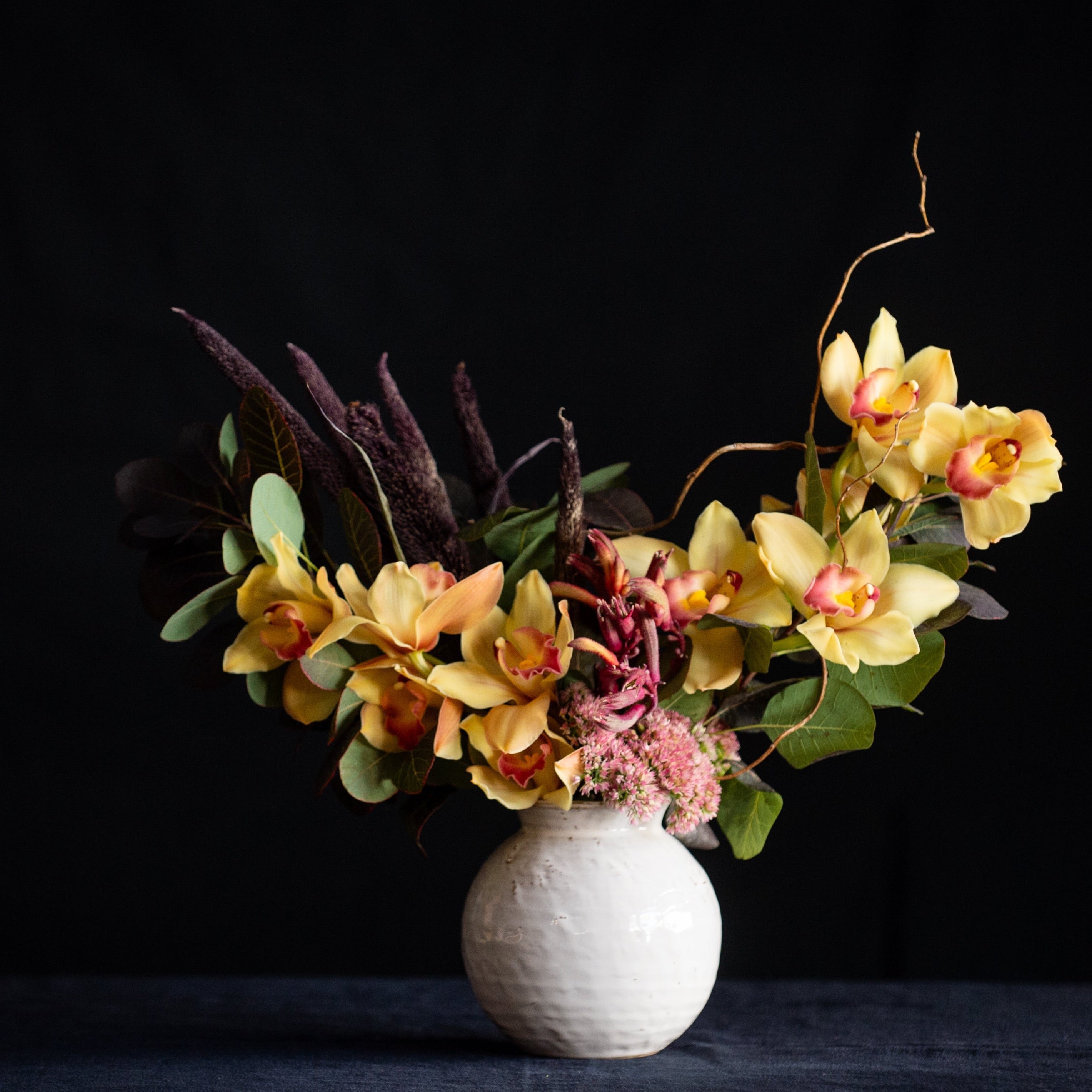 Oversized cymbidium orchid blooms, Autumn leaves, and seasonal accents make this design a great Fall go-to