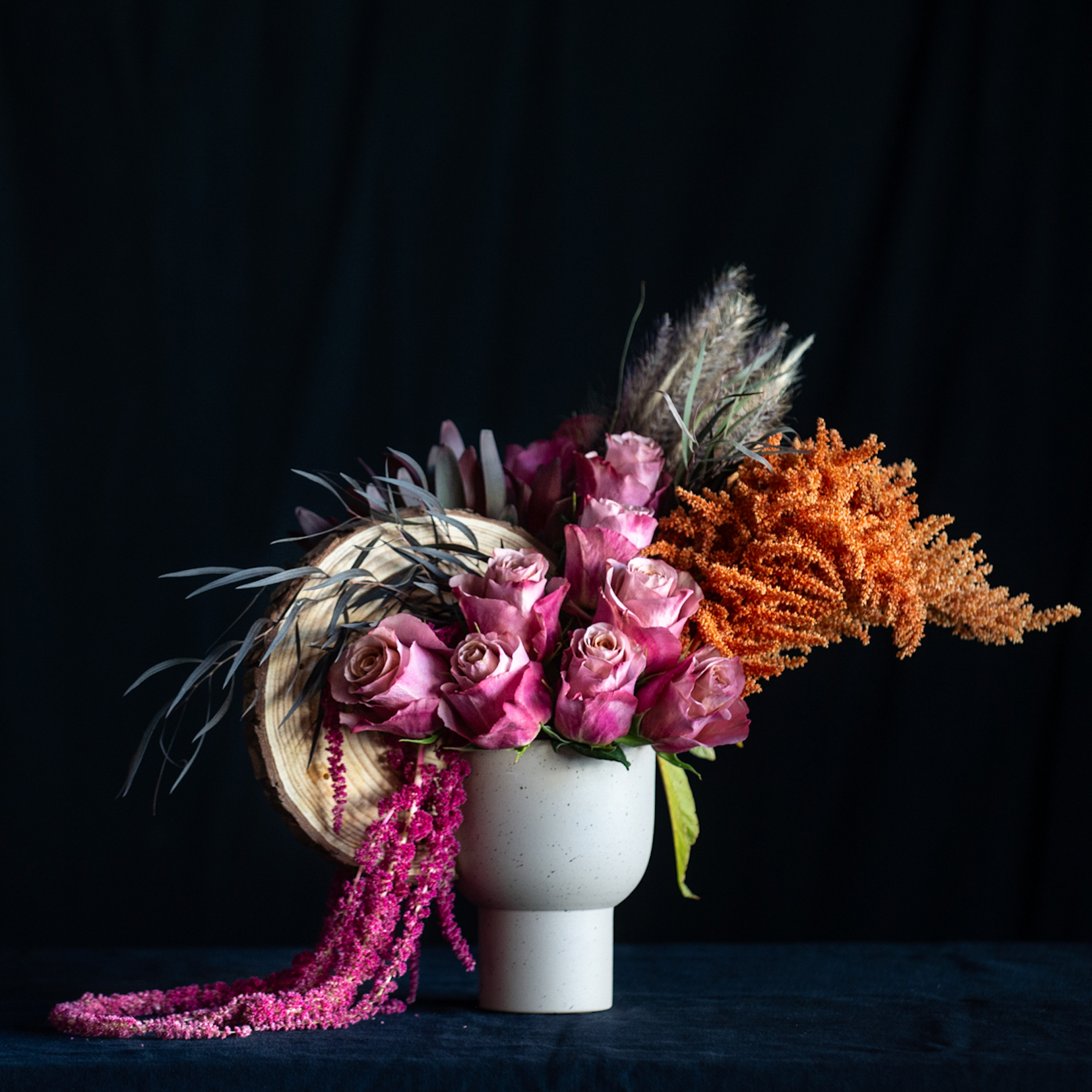 Fall floral arrangement with mauve roses, amaranthus, pampas, and autumn textures in a compote vase with wood elements.