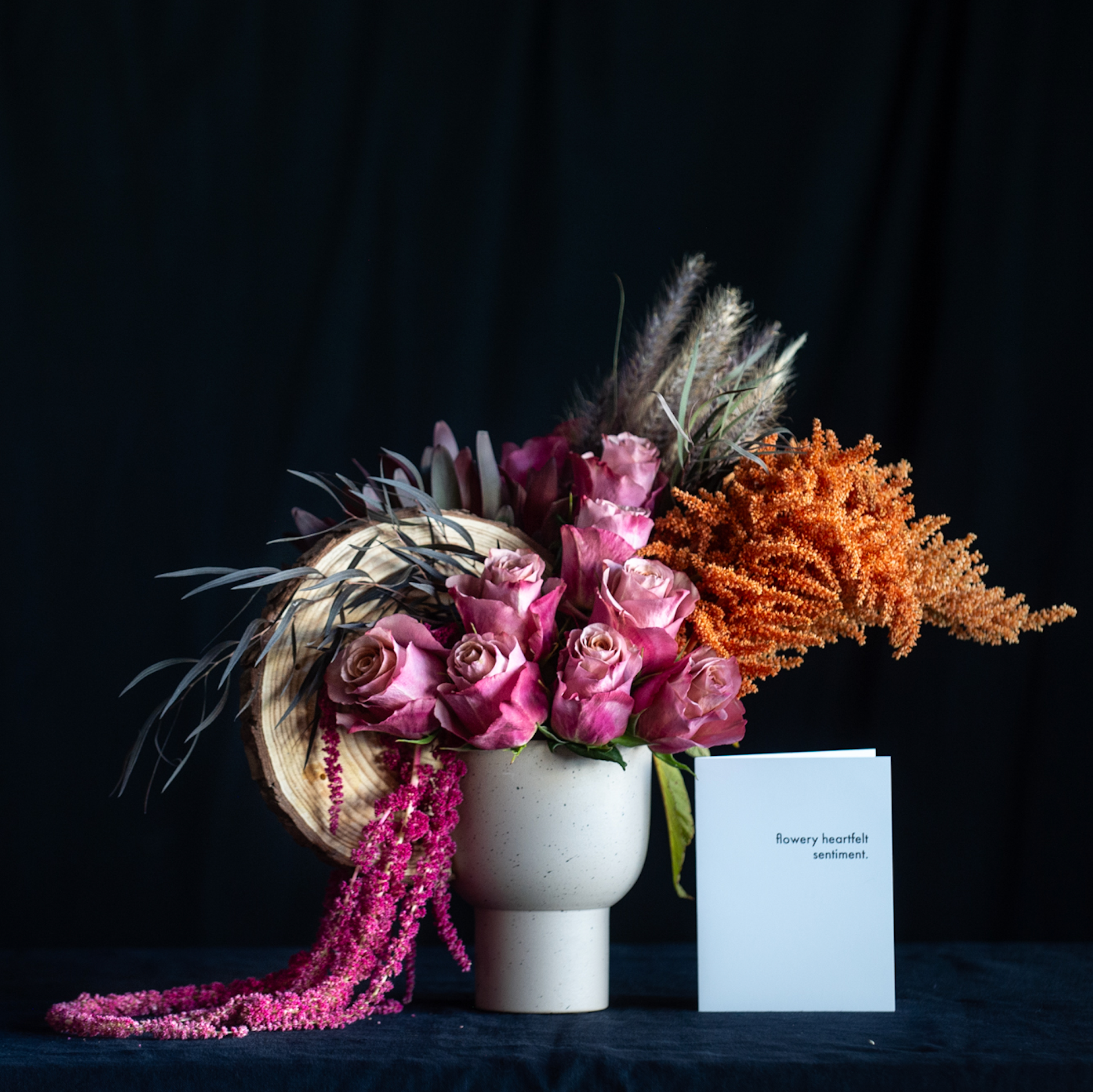Fall floral arrangement with mauve roses, amaranthus, pampas, and autumn textures in a compote vase with wood elements.