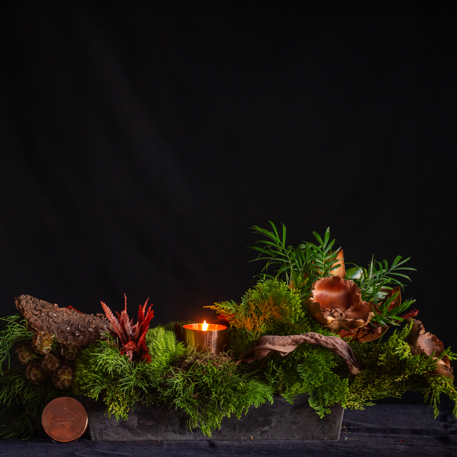 Holiday forest of greens, ferns, pods, and candlelight 