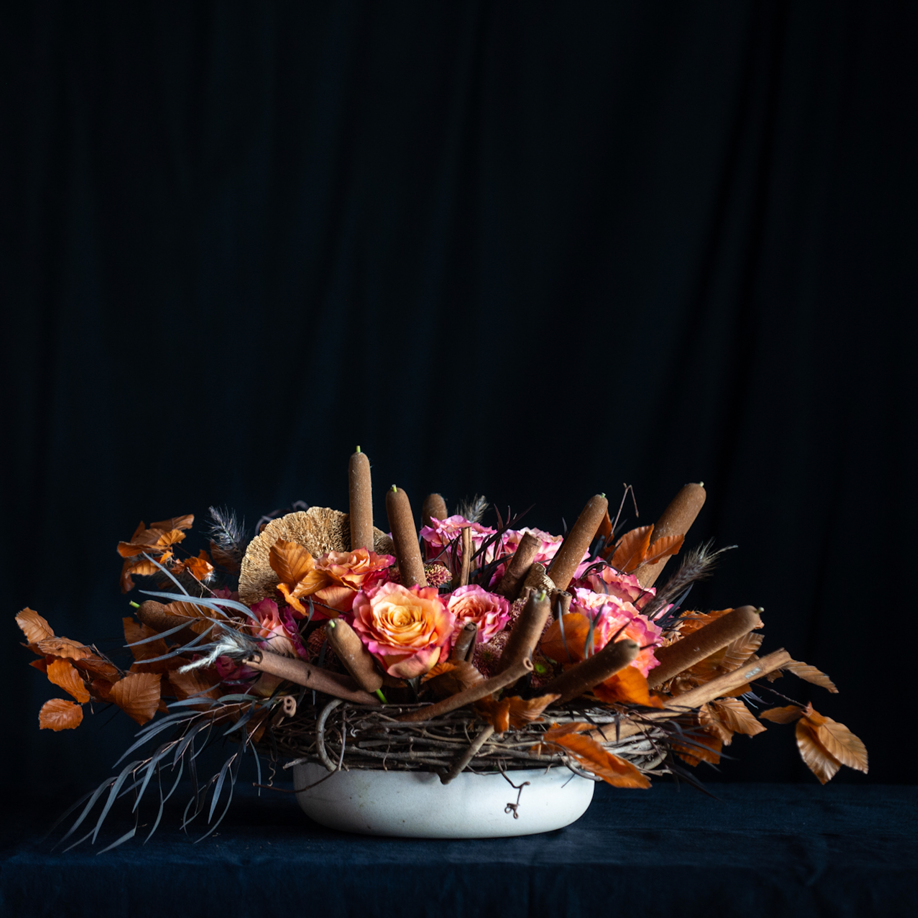 Fall floral arrangement with roses, pods, cattails, and autumn leaves in a twig nest.