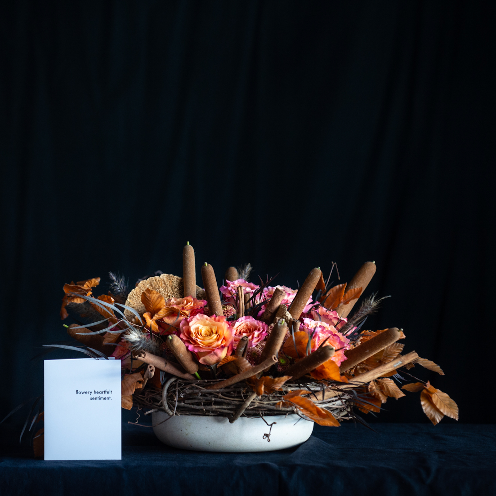 Fall floral arrangement with roses, mushroom caps, cattails, and autumn leaves in a twig nest.