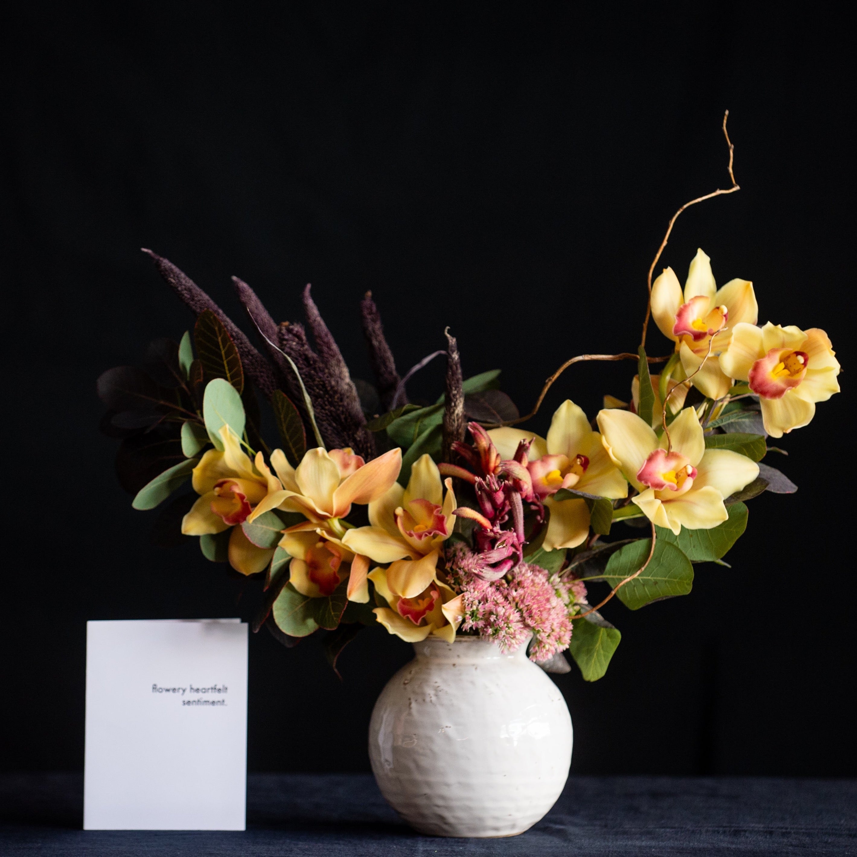 Oversized cymbidium orchid blooms, Autumn leaves, and seasonal accents make this design a great Fall go-to