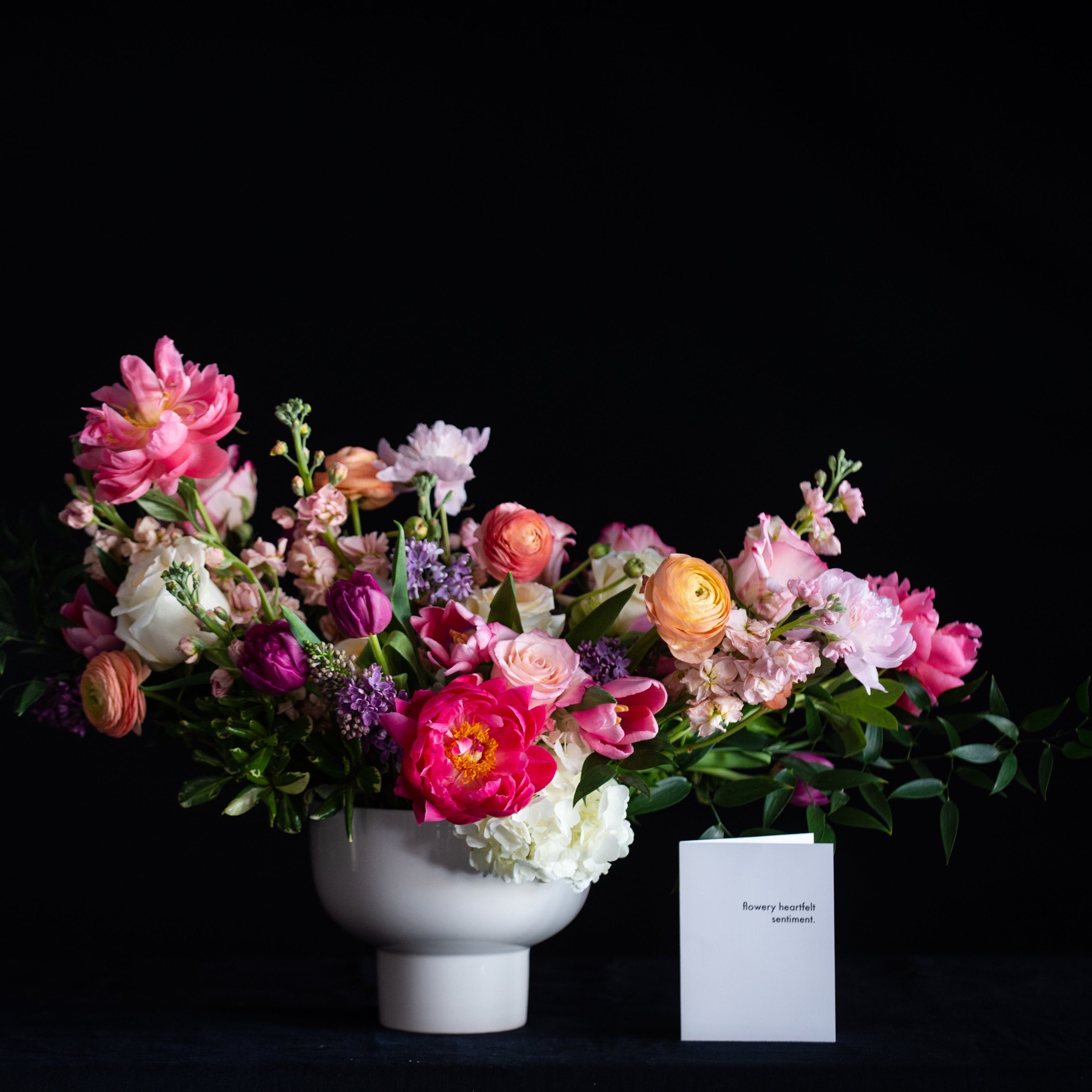 An oversized white pedestal vase is filled with the best spring stems - hydrangea, roses, ranunculus, tulips, lilac, and peonies. 