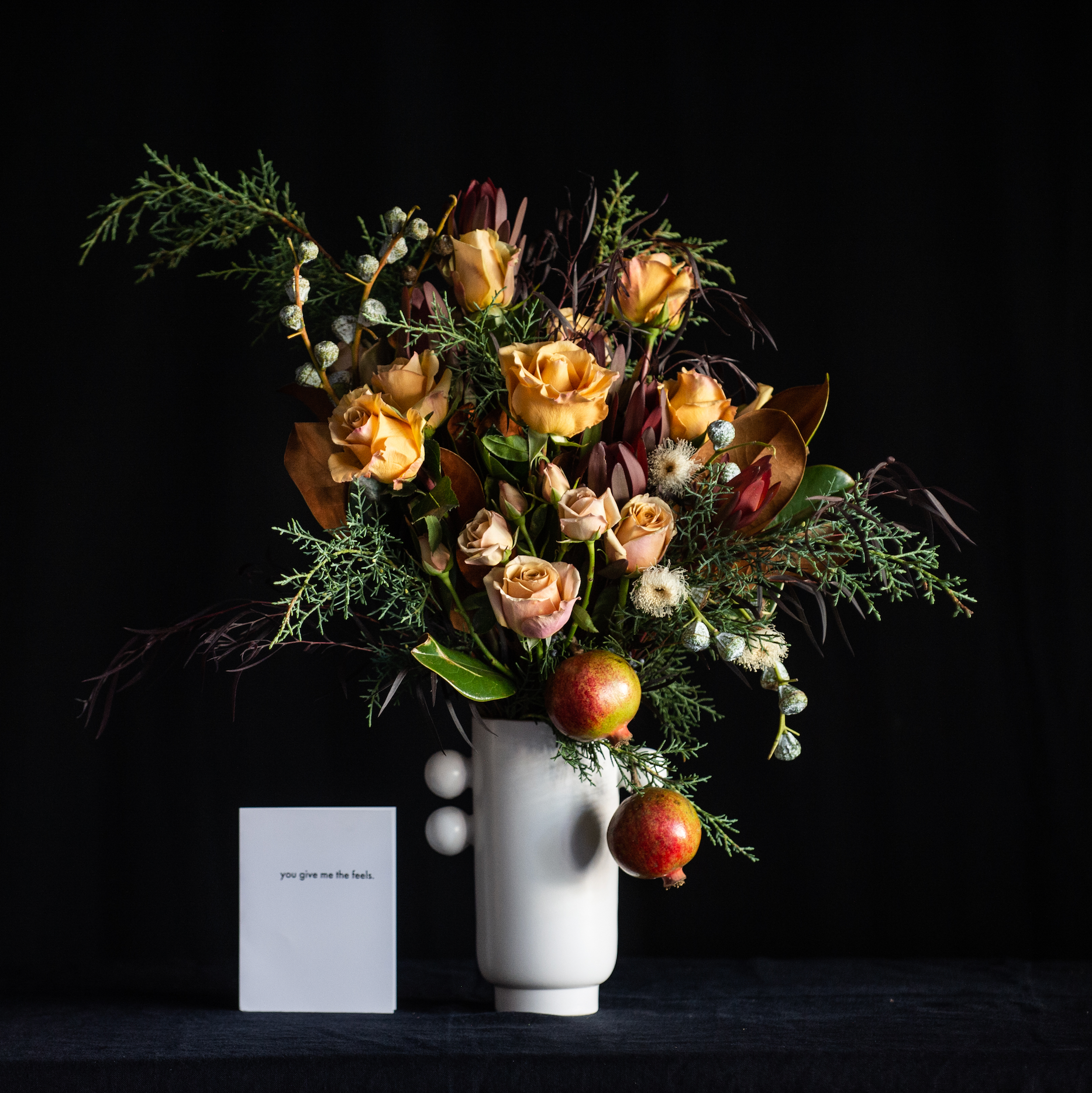 Festive holiday forest design with dozen golden roses, burgundy accents, holiday greens, magnolia, and pomegranate