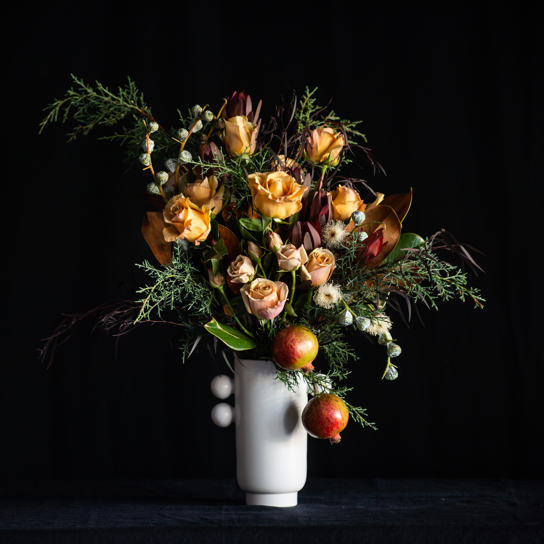 Winter forest floral design of a dozen golden roses, burgundy accents and a pomegranate