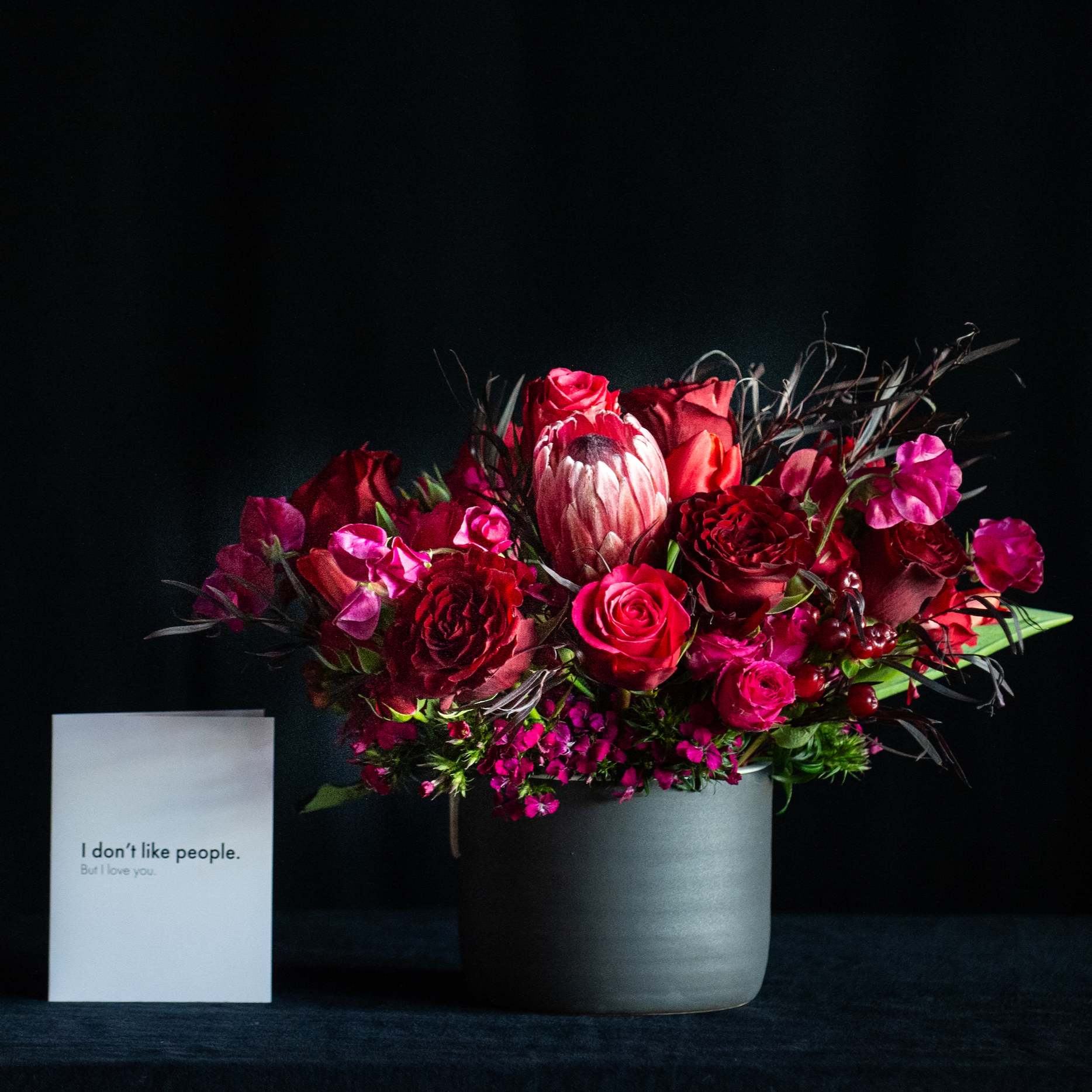 Red roses in a black container with chocolate brown foliage and tropicals