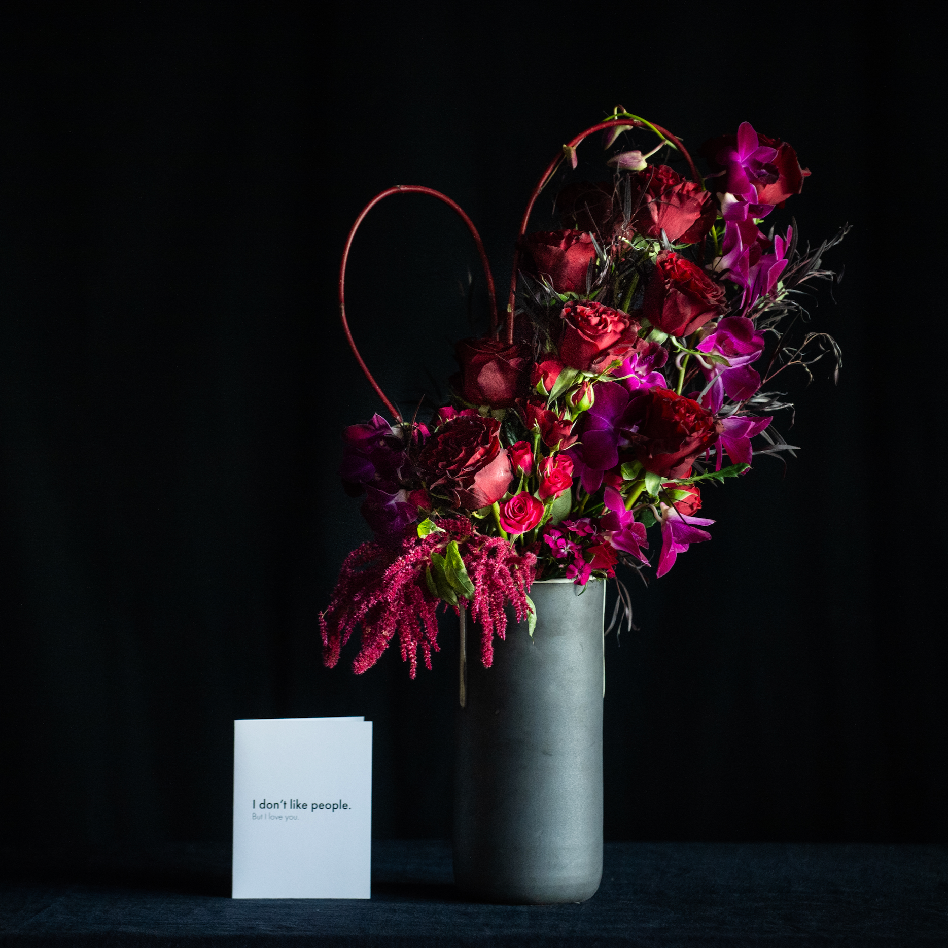 Red roses in a black matte ceramic vase with orchids