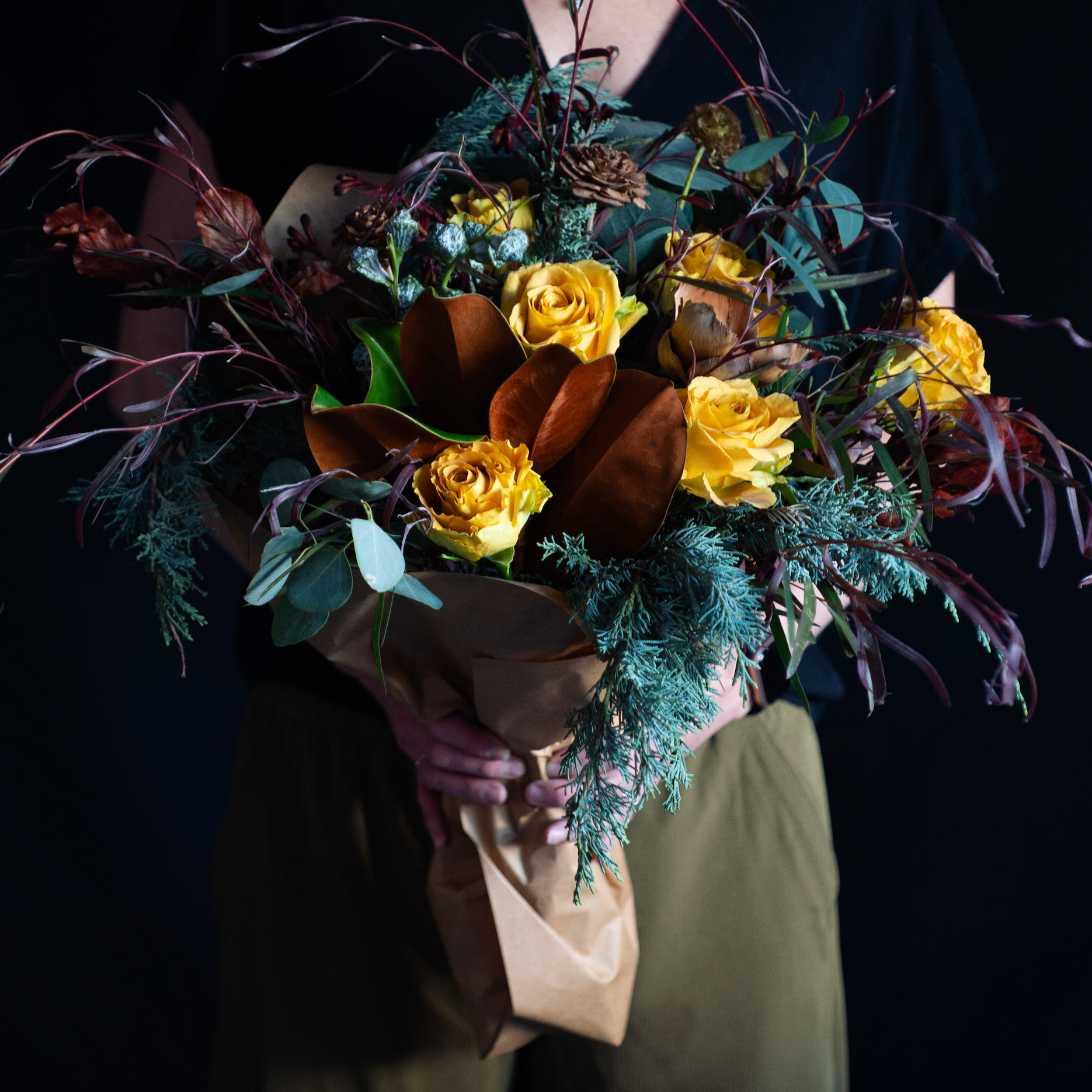 wild winter bouquet of golden roses and winter greenery with magnolia