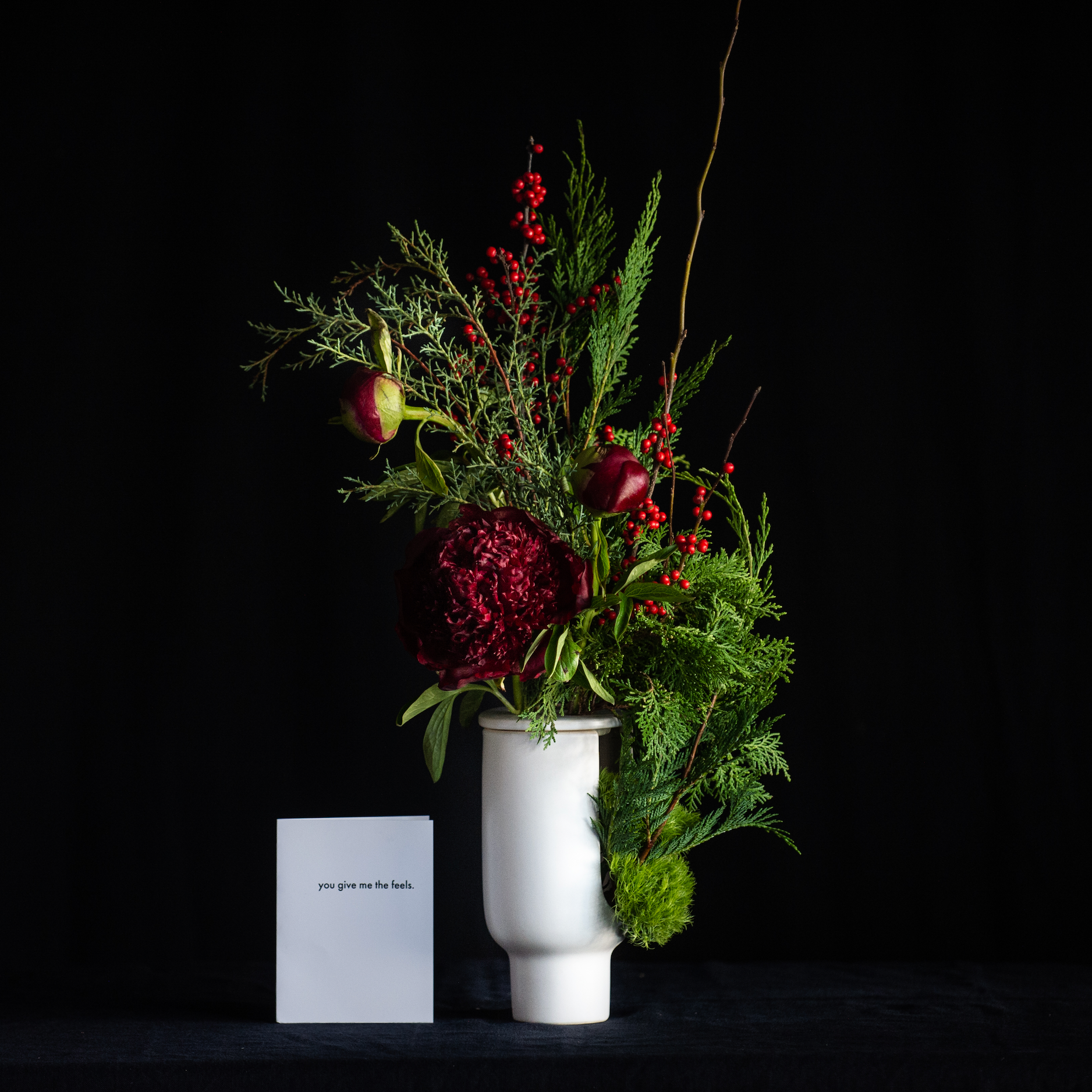 Peony flowers and holiday greens in a modern flower frog vase