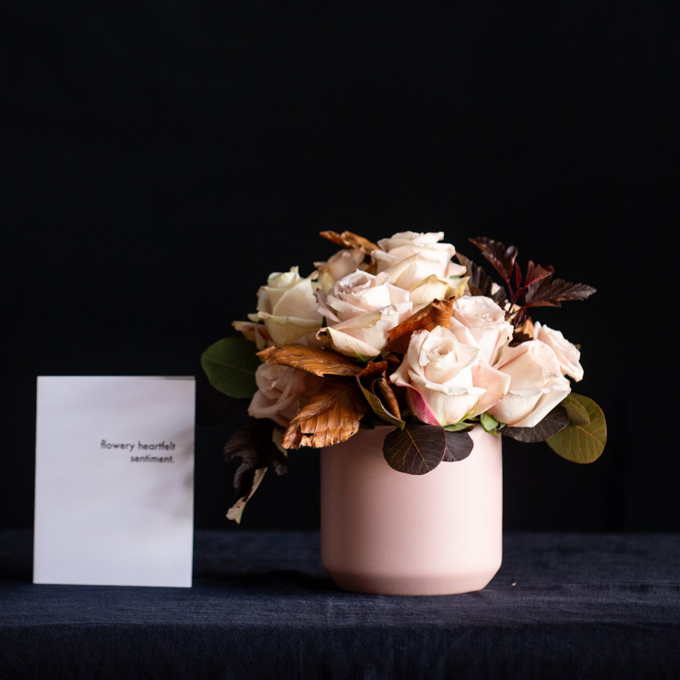 A dozen taupe roses with fall foliage in a matte blush container