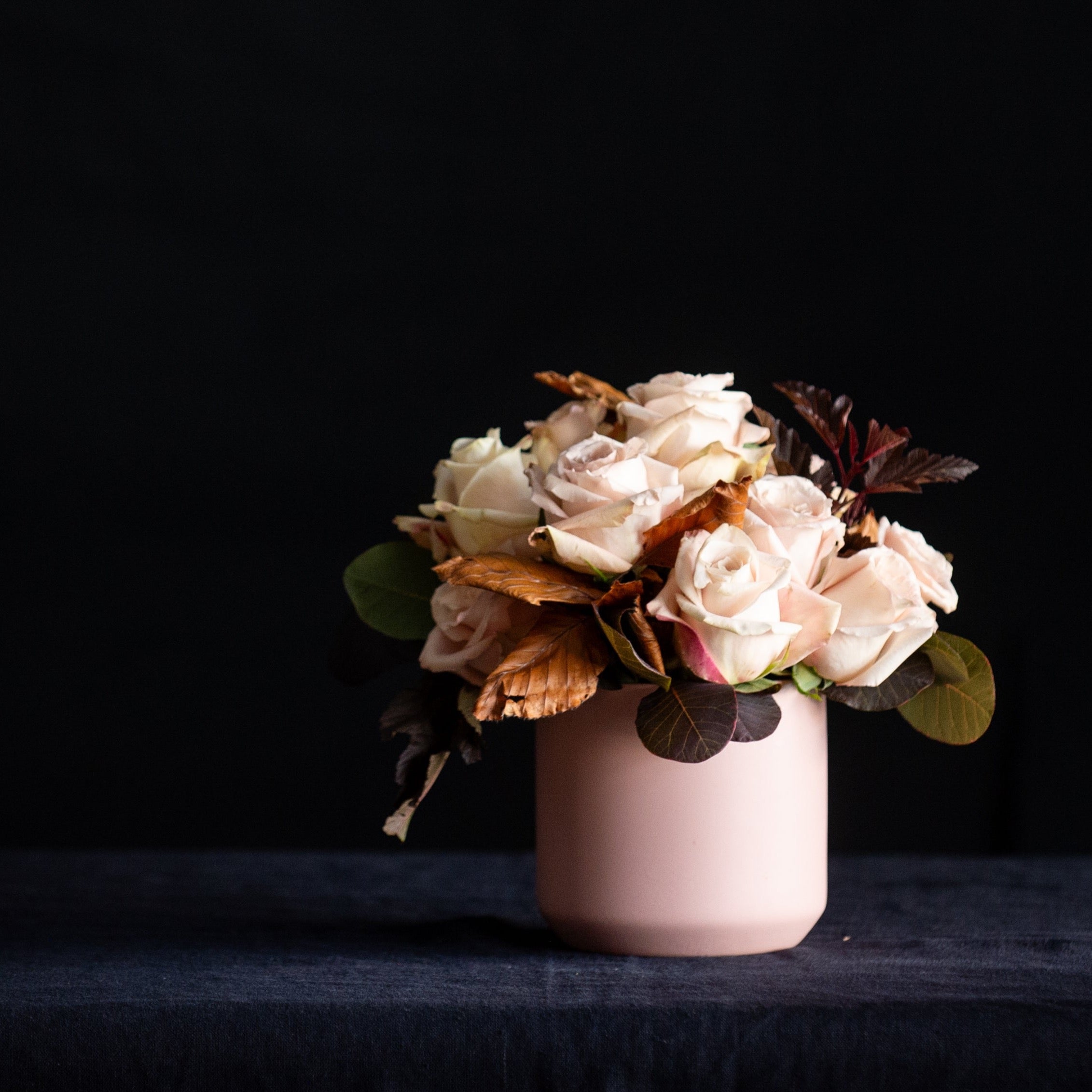 A dozen taupe roses with fall foliage in a matte blush container
