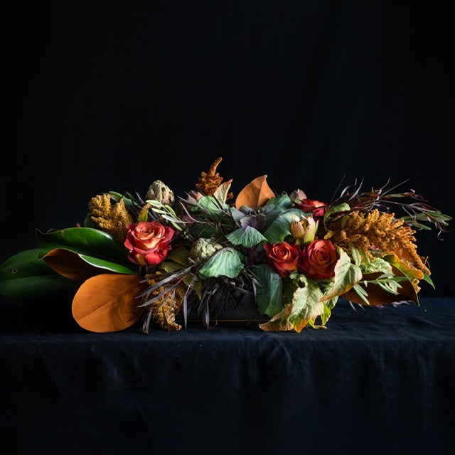 Thanksgiving Punch is a long fall arrangement featuring roses, kale, fall stems, and magnolia leaves. Colors: Reds, Taupes, Brown