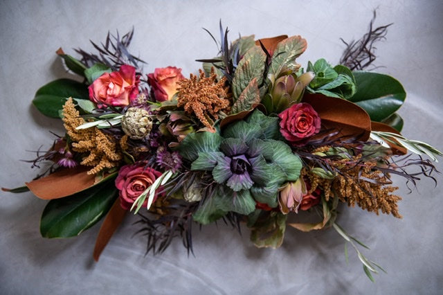 Thanksgiving flower arrangement of magnolia leaves, kale, roses, artichokes, and textural seasonal stems