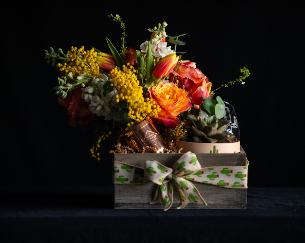 A curated gift box with desert / Arizona elements. Bright florals, an Arizona made candle, a desert plant, and a cactus etched glassware