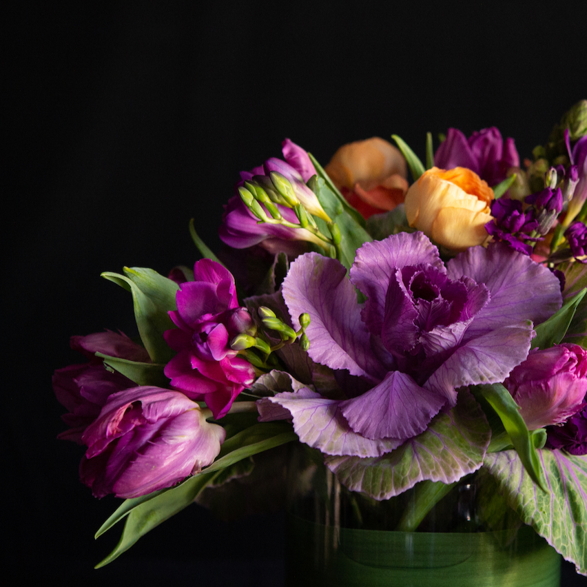 An asymmetrical design of kale, freesia, ranunculus, and snapdragons in a leaf lined container. Made by a local florist. 