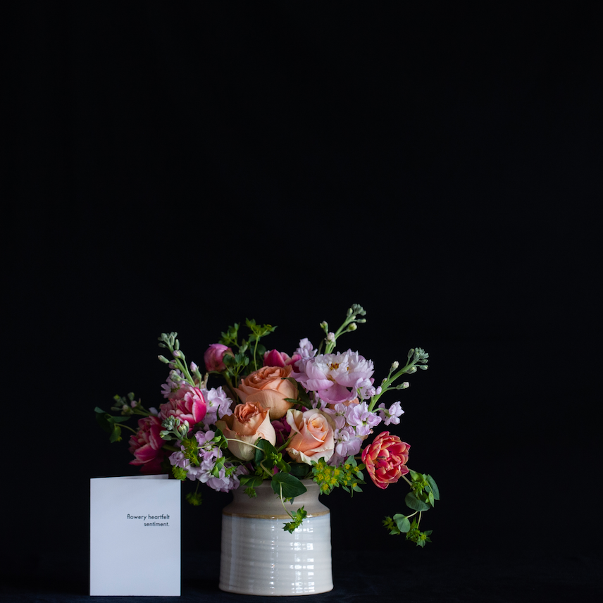 A design of roses, hydrangea, stock and tulips in a pottery inspired ceramic container.