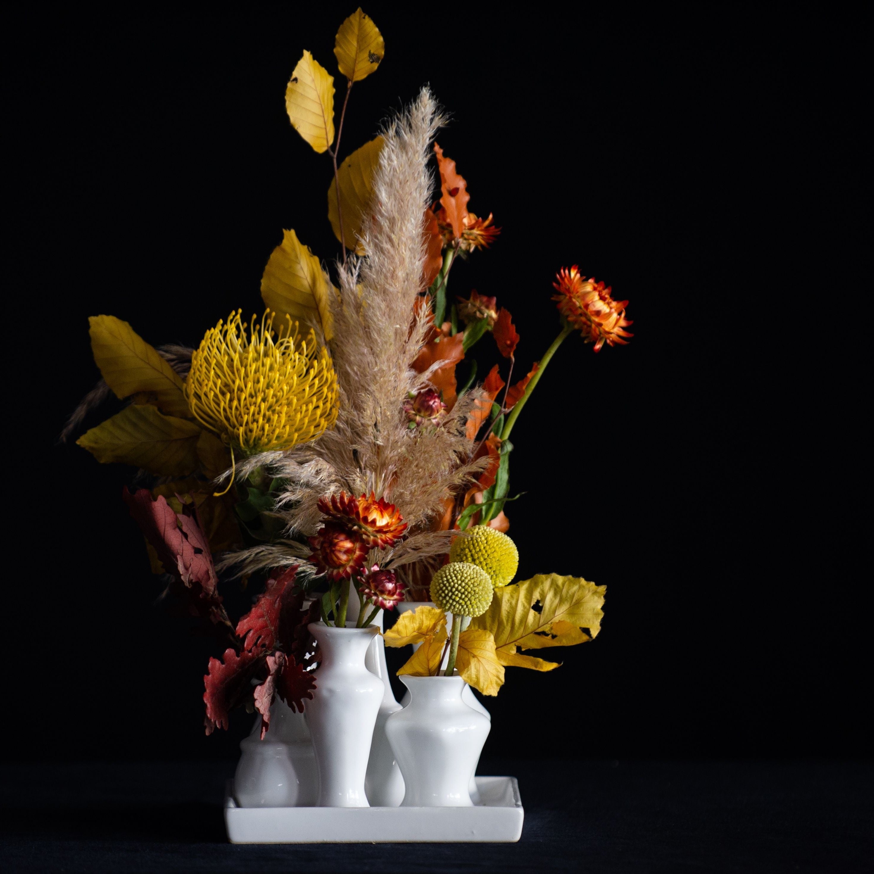 A collection of white ceramic bud vases on a tray filled with seasonal stems. 