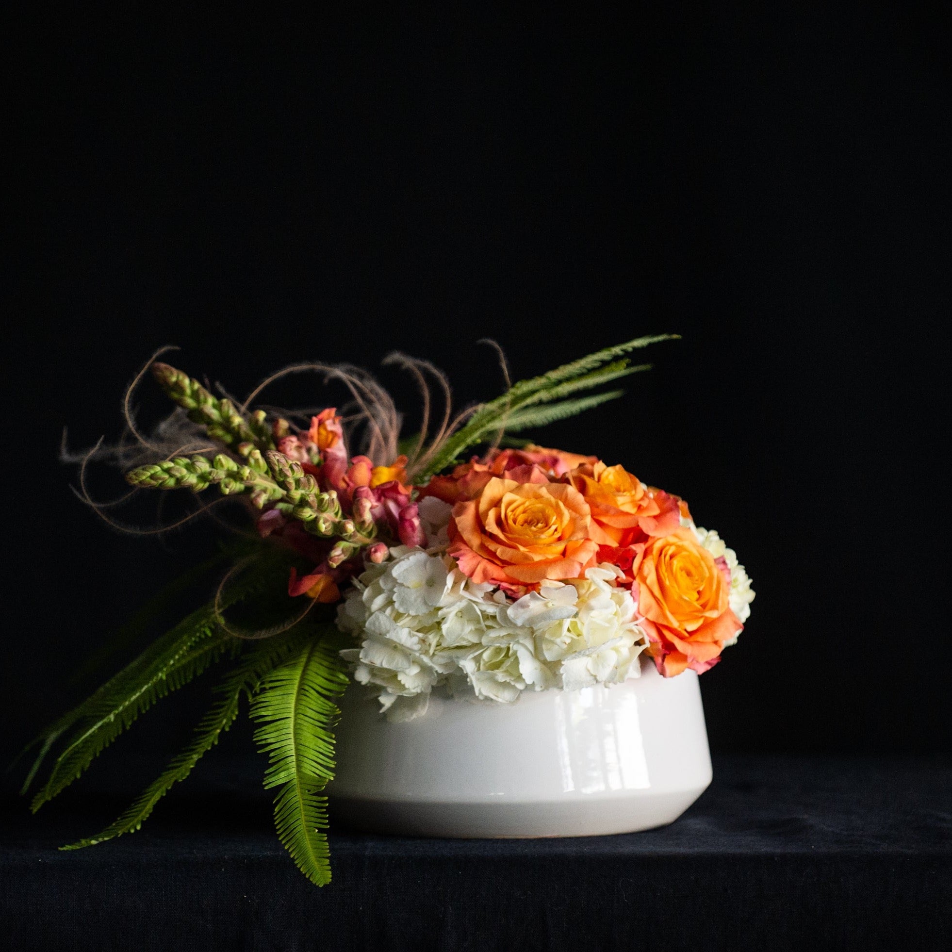 Filled with white hydrangea, orange roses, and salmon snapdragons it's all about peachy perfection in a white ceramic bowl