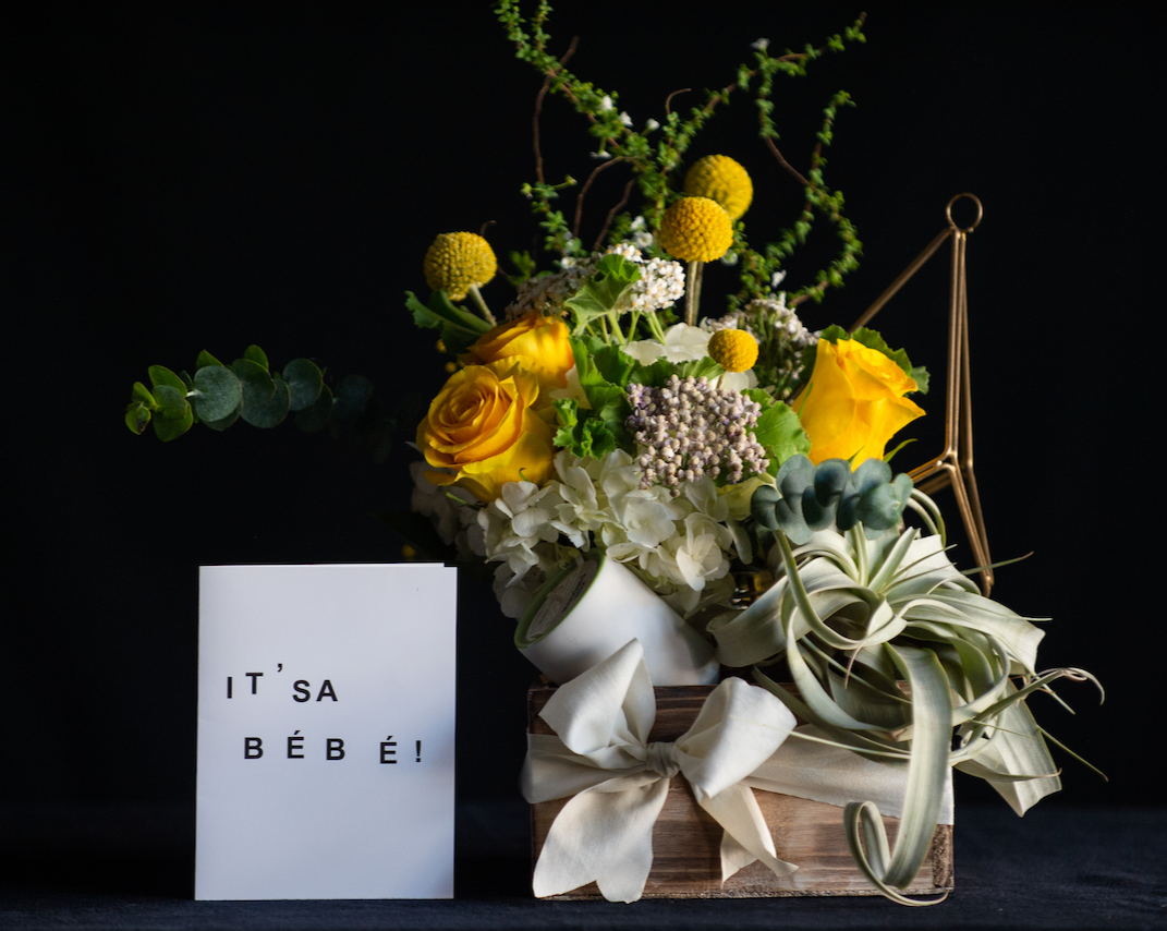 A gift box for new parents with a floral arrangement, candle, and low maintenance plant