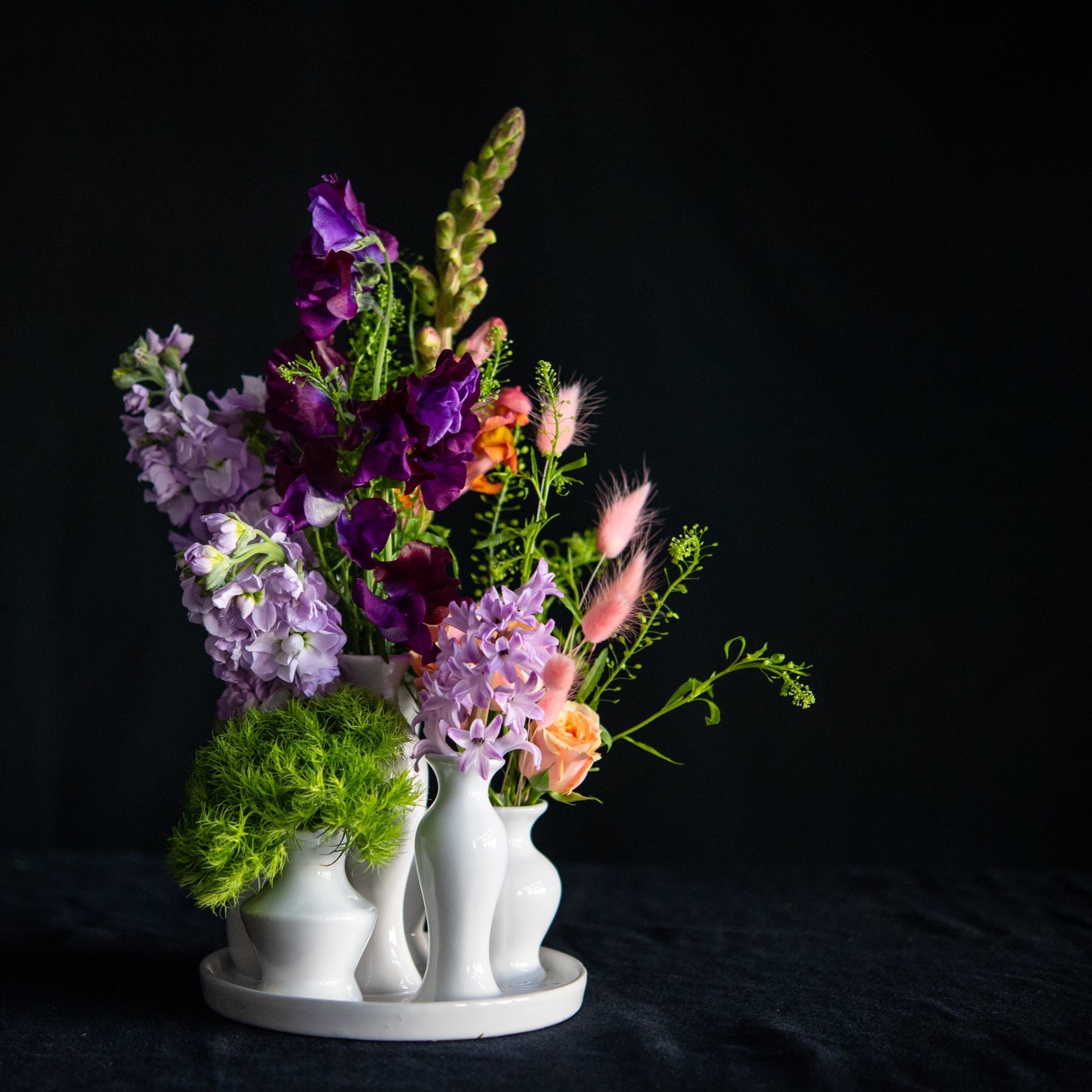 A collection of white ceramic bud vases filled with premium seasonal stems for any day