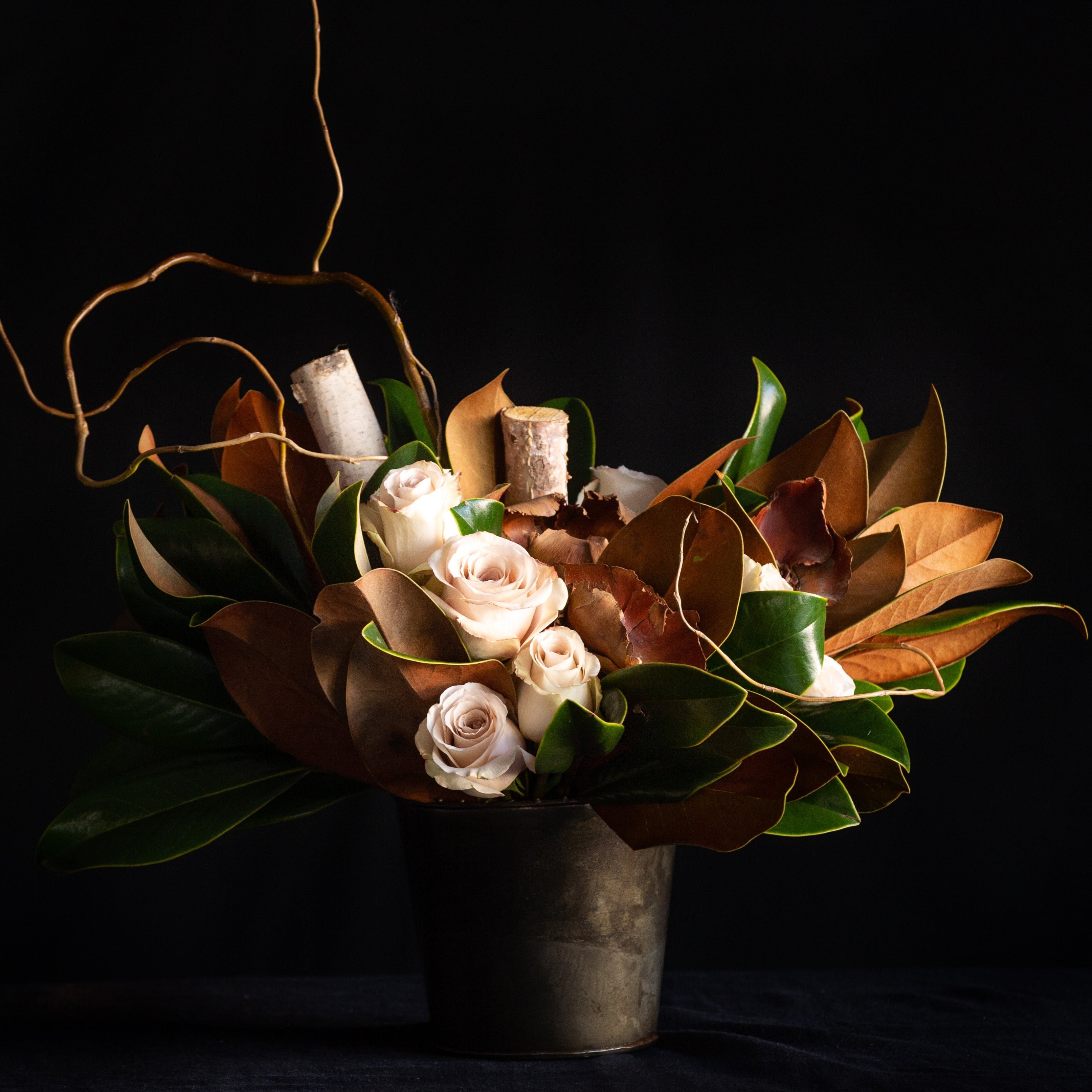 Taupe roses nestled in between magnolia leaves, birch, and curly willow. All around design. created by a local florist