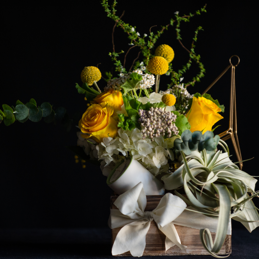 A gift box for new parents with a floral arrangement, candle, and low maintenance plant