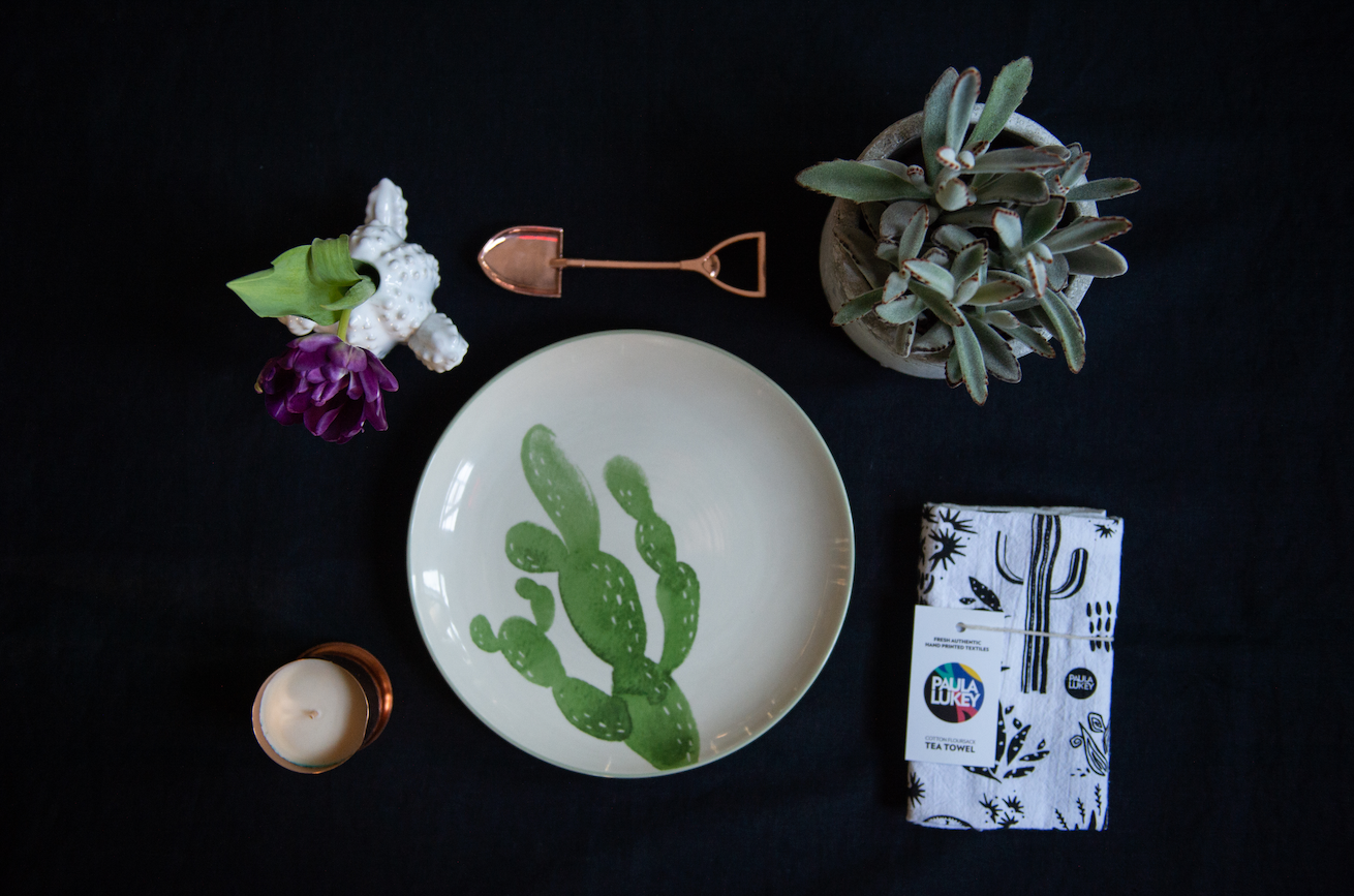 Housewarming gift of a tea towel, bottle opener, bud vase, plant, and desert plate plus a locally made hand poured candle.