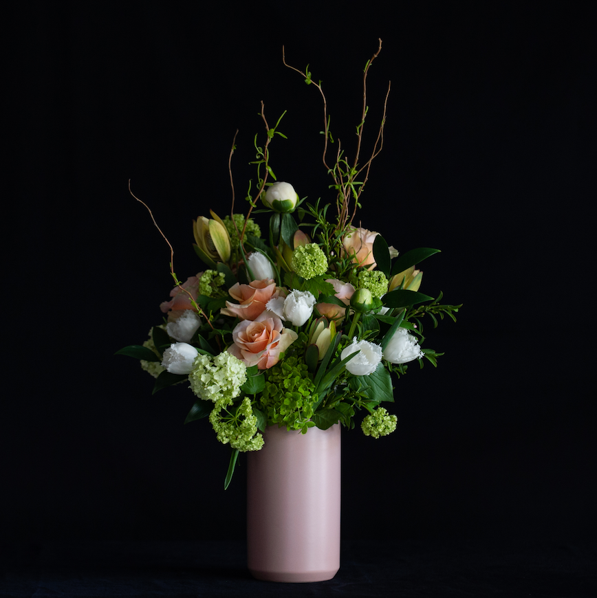 A tall floral design for mother's day of peach, white and green Spring stems.