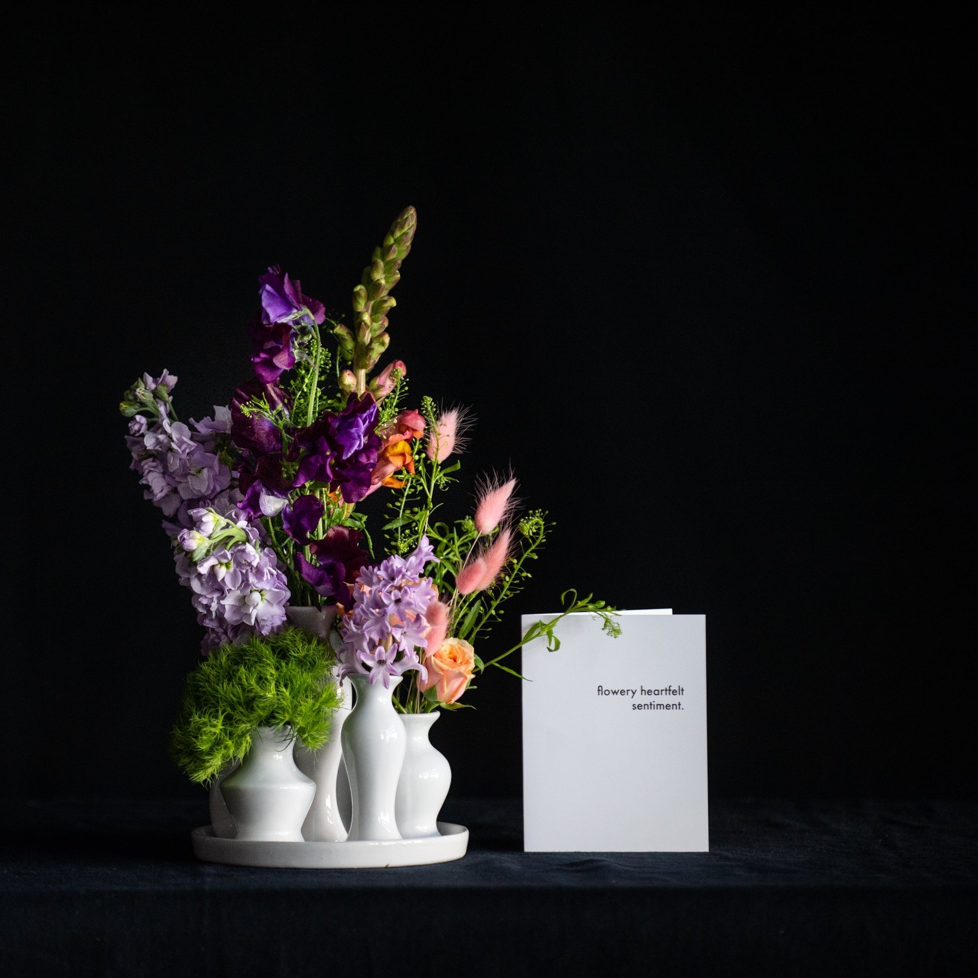 A collection of white ceramic bud vases filled with premium seasonal stems for any day