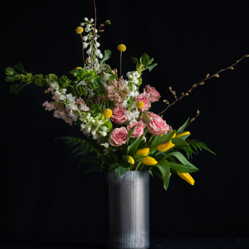 Tall Spring floral design of a dozen roses, tulips, larkspur, stock, and blooming branches. 