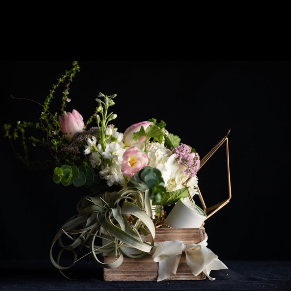 a gift box filled with a floral arrangement, candle and low maintenance plant